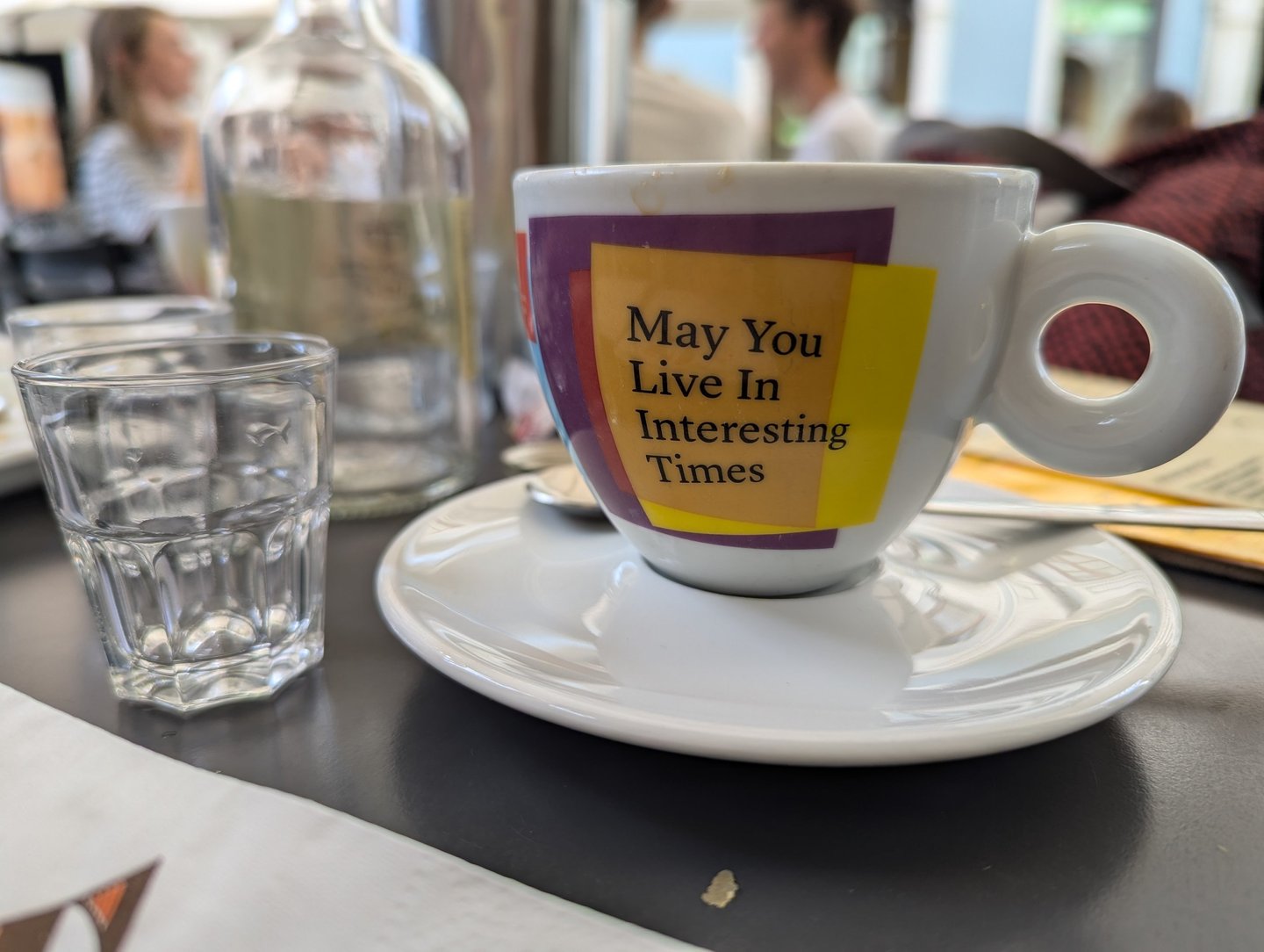 A coffee cup on a table, with the text 'May you live in interesting times' written on the cup.