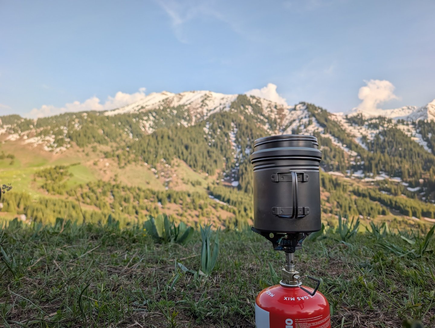 Portable camping stove and Vargo BOT on a grassy mountain ridge with snowy peaks in the background.