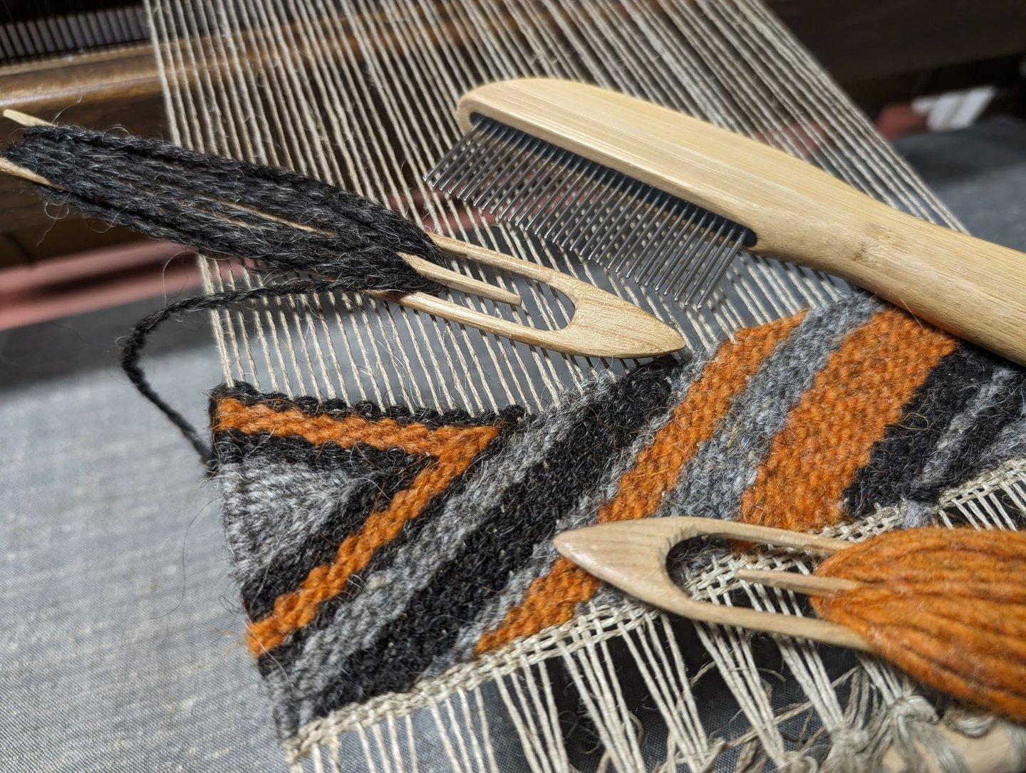 a weaving loom with shuttle, combe and black grey orange wool  threads on a navajo rug in progress