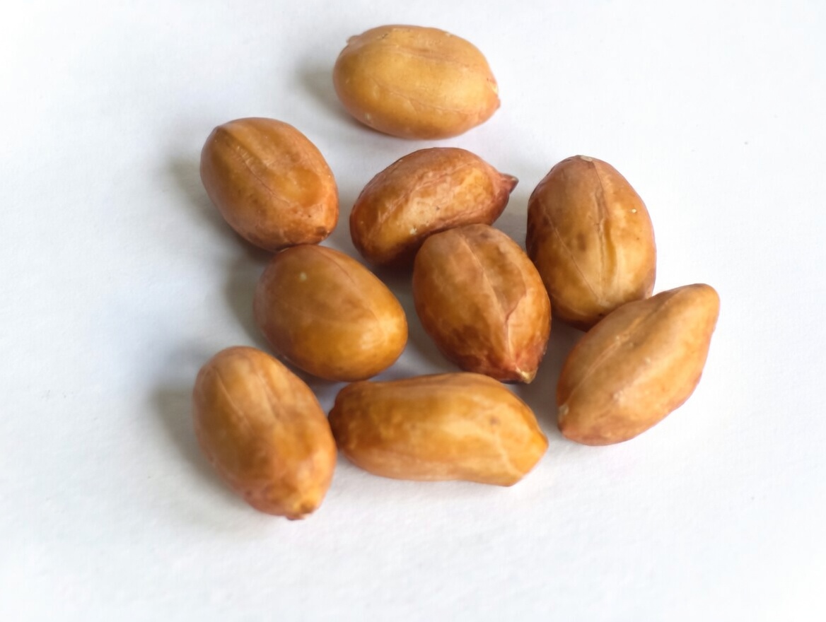 A small cluster of raw shelled peanuts scattered on a plain white surface.