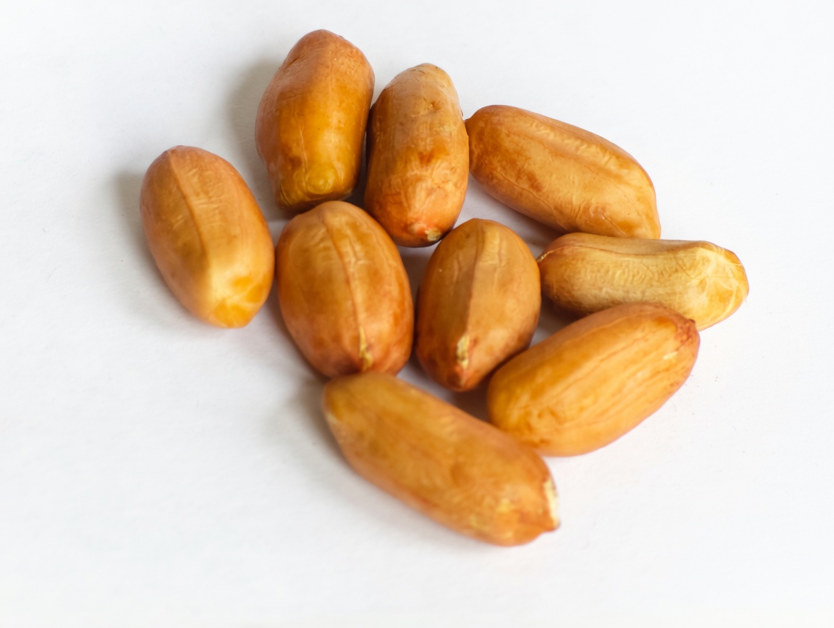 A small pile of shelled raw peanuts with red skins isolated on a white background.