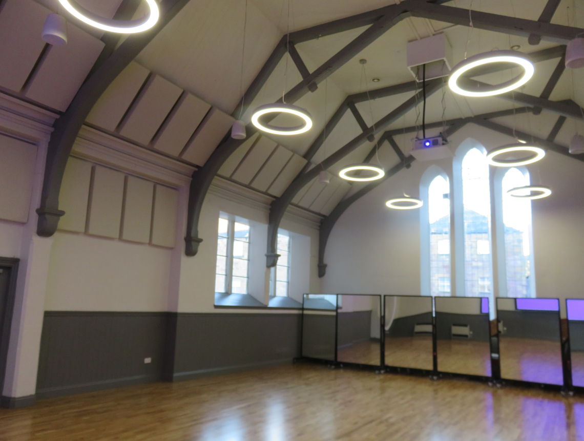 A large well-lit hall with a vaulted ceiling and large windows. It has a flat wood floor.