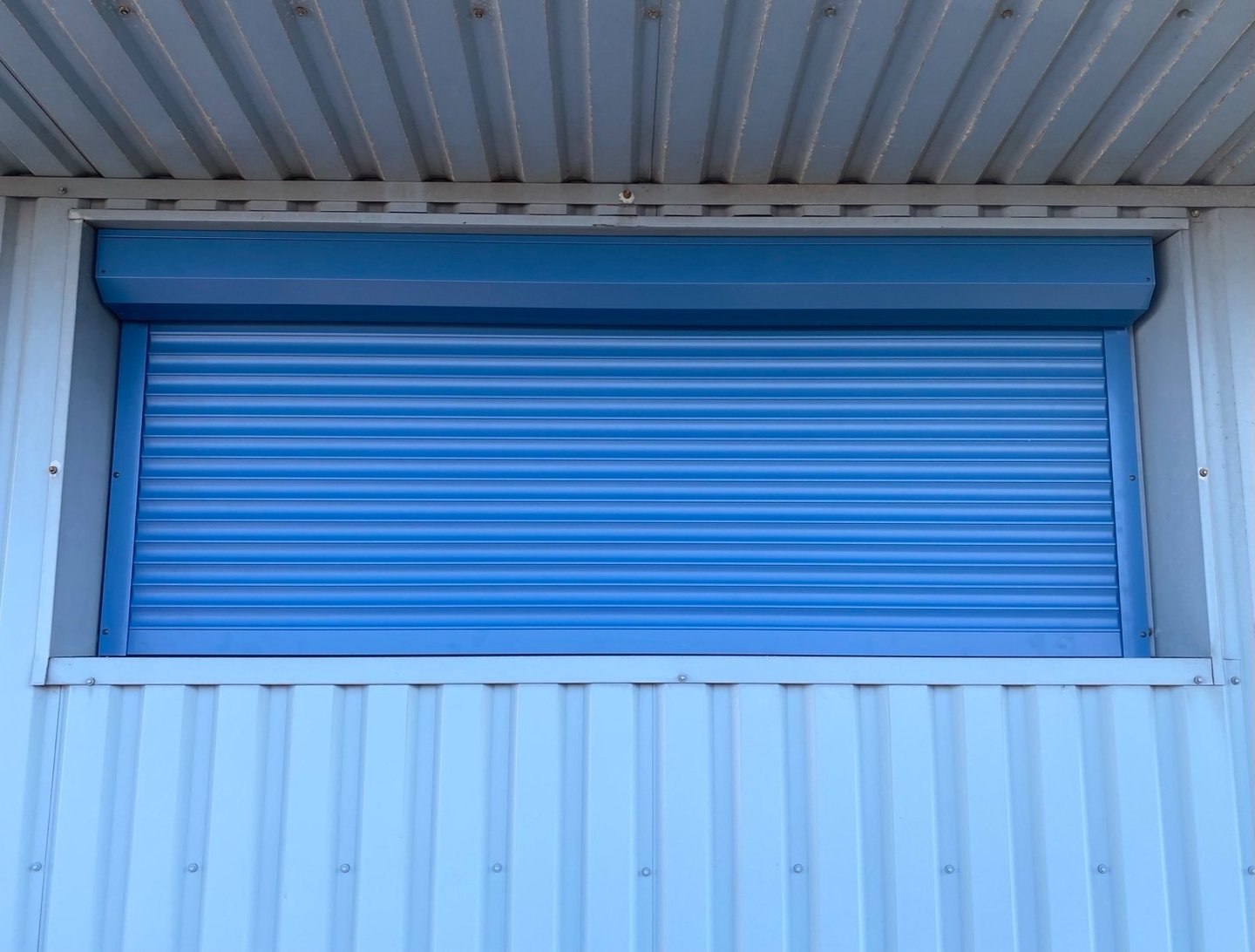 šiame paveikslėlyje matomos apsauginės žaliuzės mėlynos spalvos sumontuotos ant lango