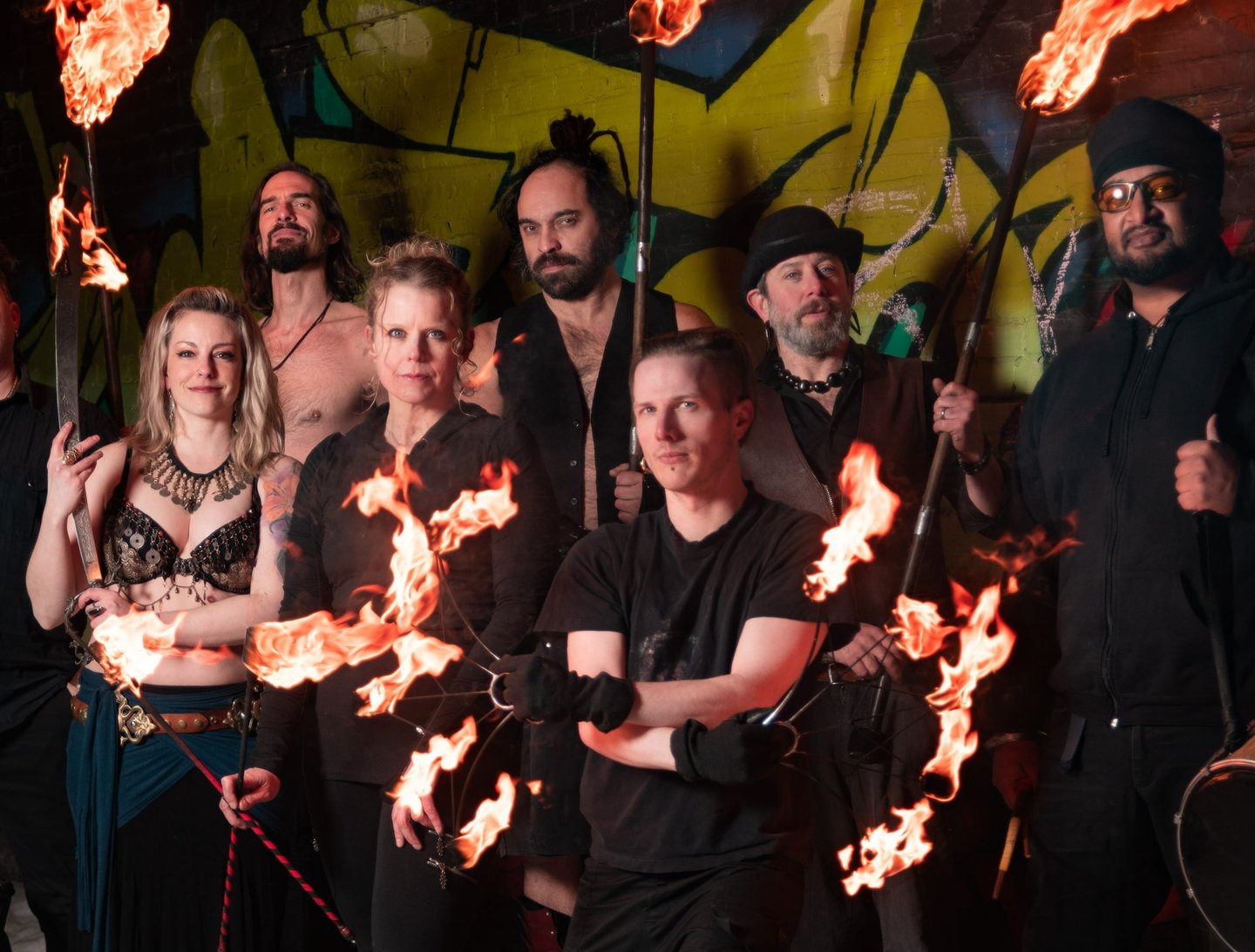 Flame Syndicate poses in front of a wall full of graffiti art