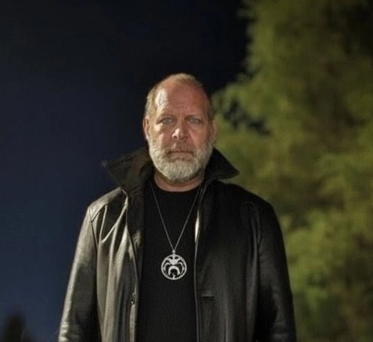 the founder standing outside at night in a black leather jacket and black low collared shirt.