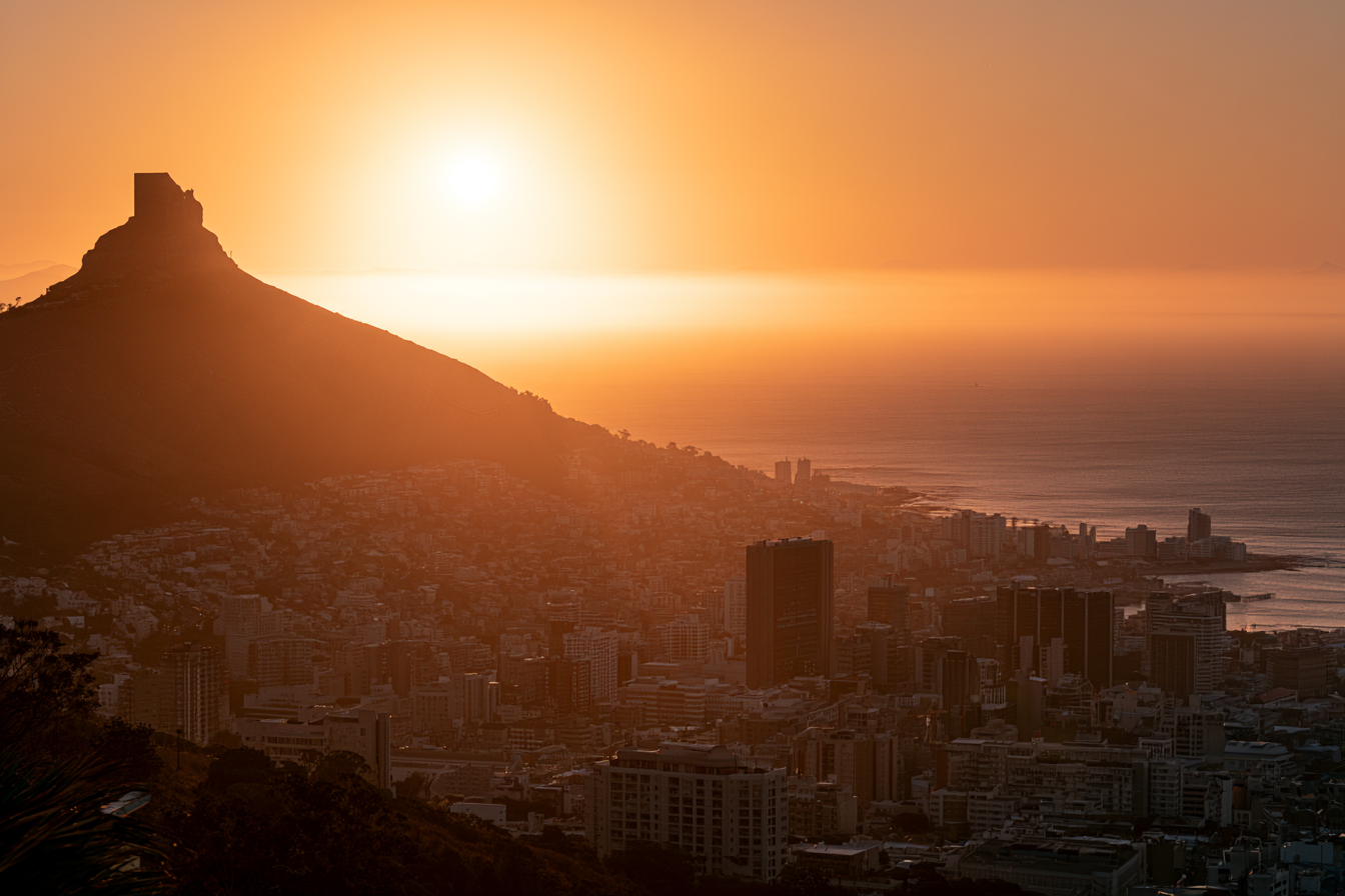 Golden sunset over Cape Town city skyline with Lion's Head mountain and Atlantic Ocean.