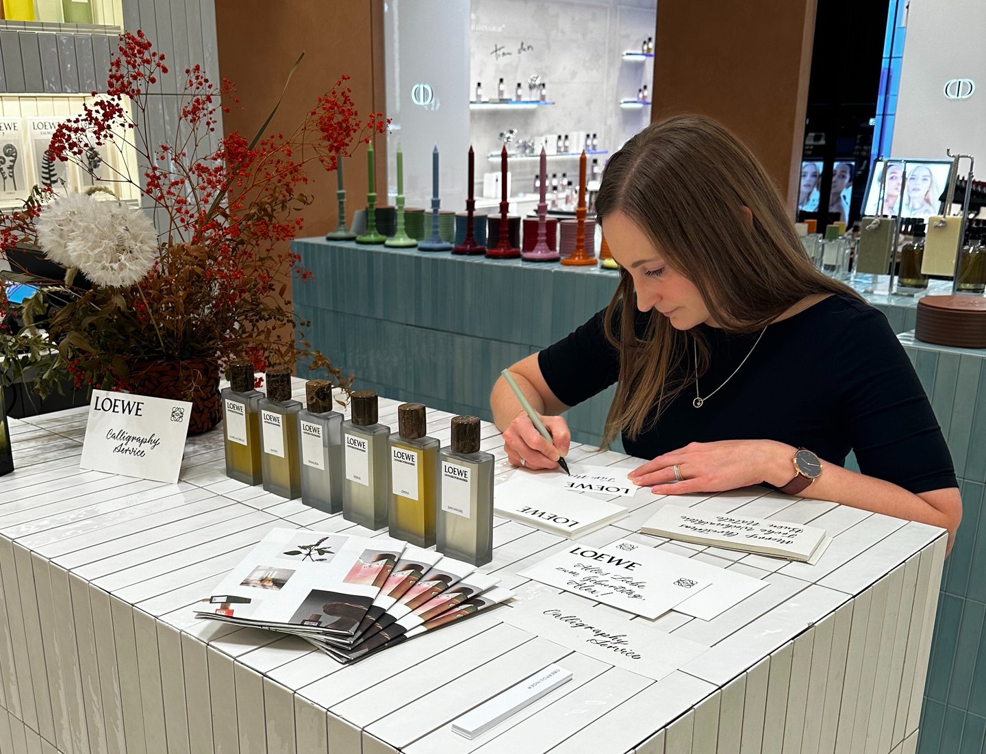 A calligrapher provides hand-lettered personalization for Loewe perfumes at a luxury fragrance counter.