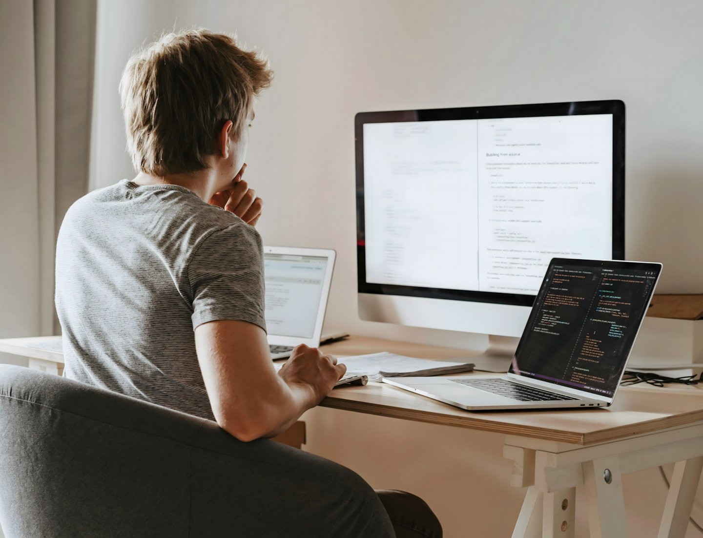 Un homme assis à un bureau avec deux ordinateurs portables et un iMac devant lui