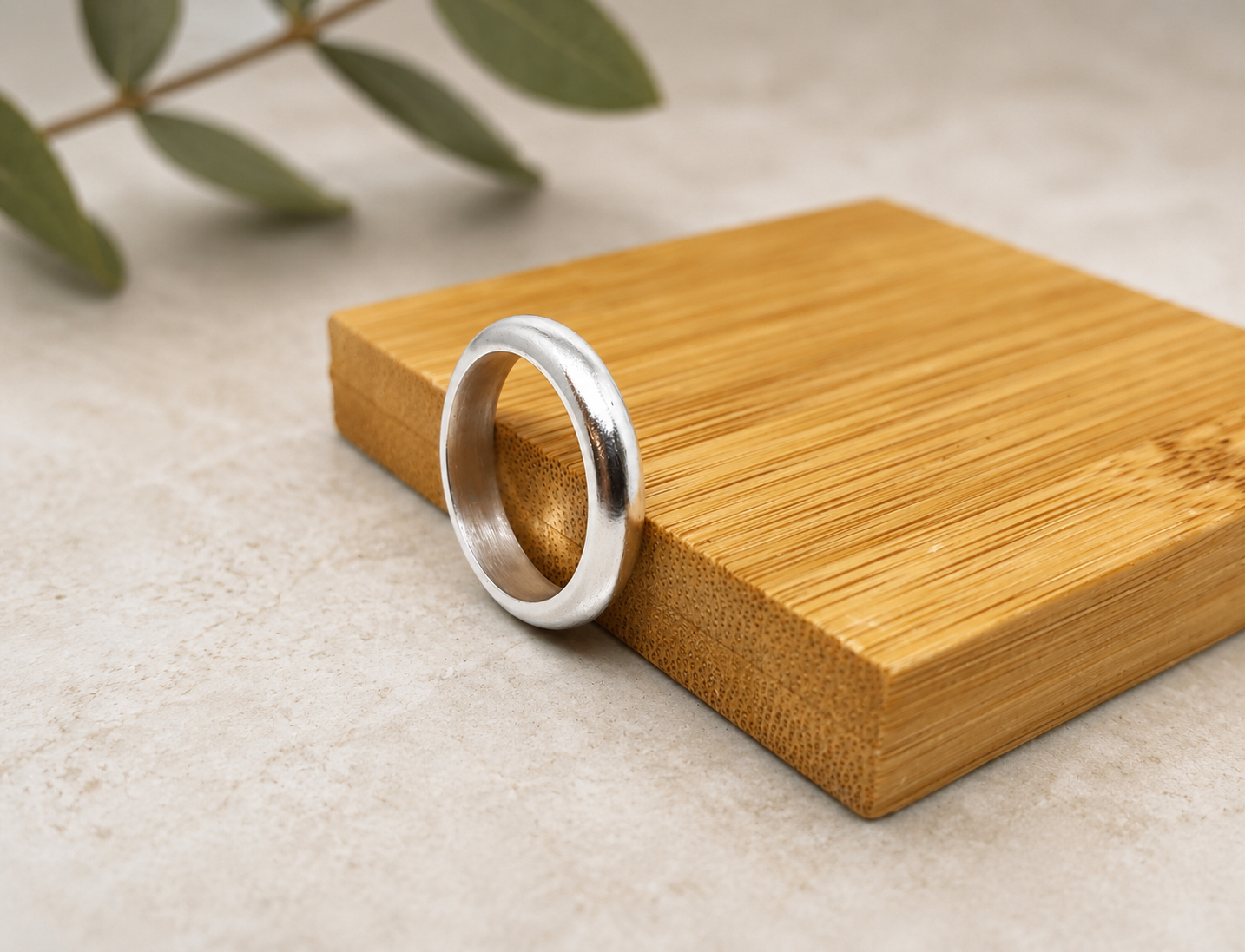 Minimalist polished satin 999 fine silver wedding band  on a bamboo display block in green leaves.