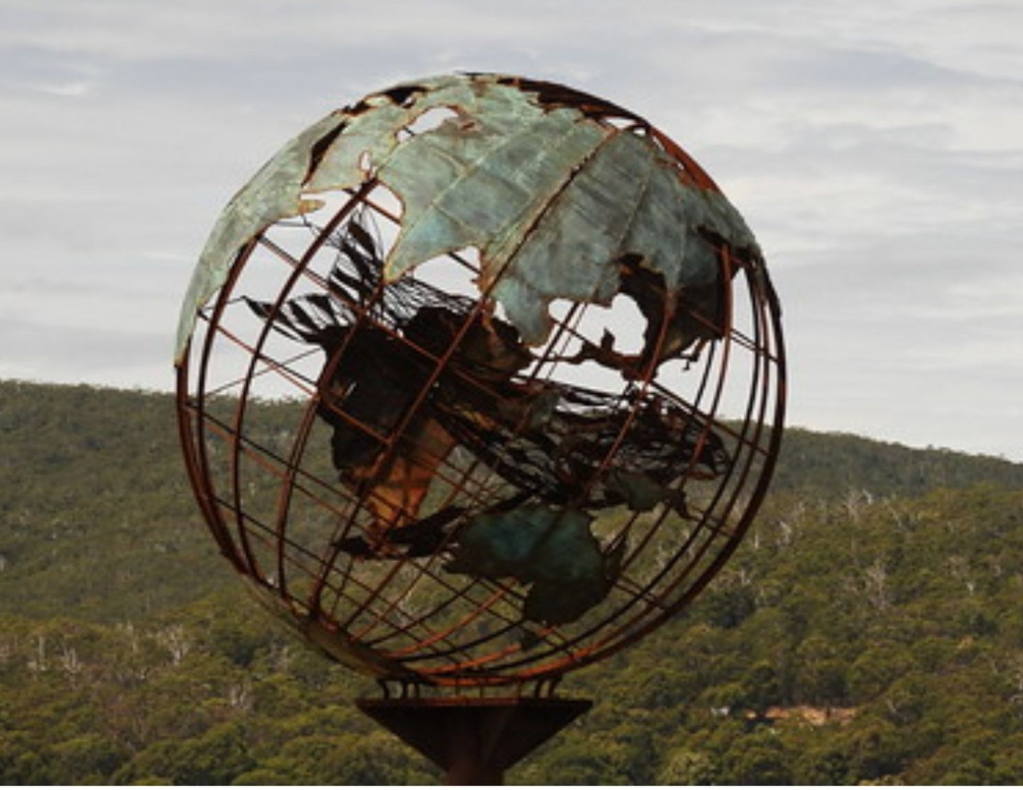 Verdigris metal globe sculpture on the beach with a mother whale and her calf in the middle of it