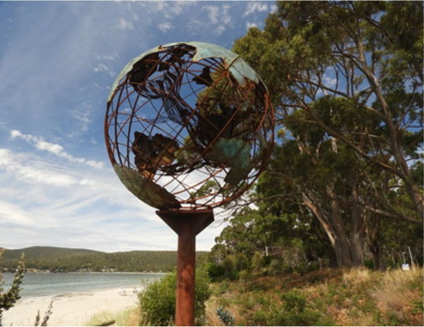 Verdigris metal globe sculpture on the beach with a mother whale and her calf in the middle of it