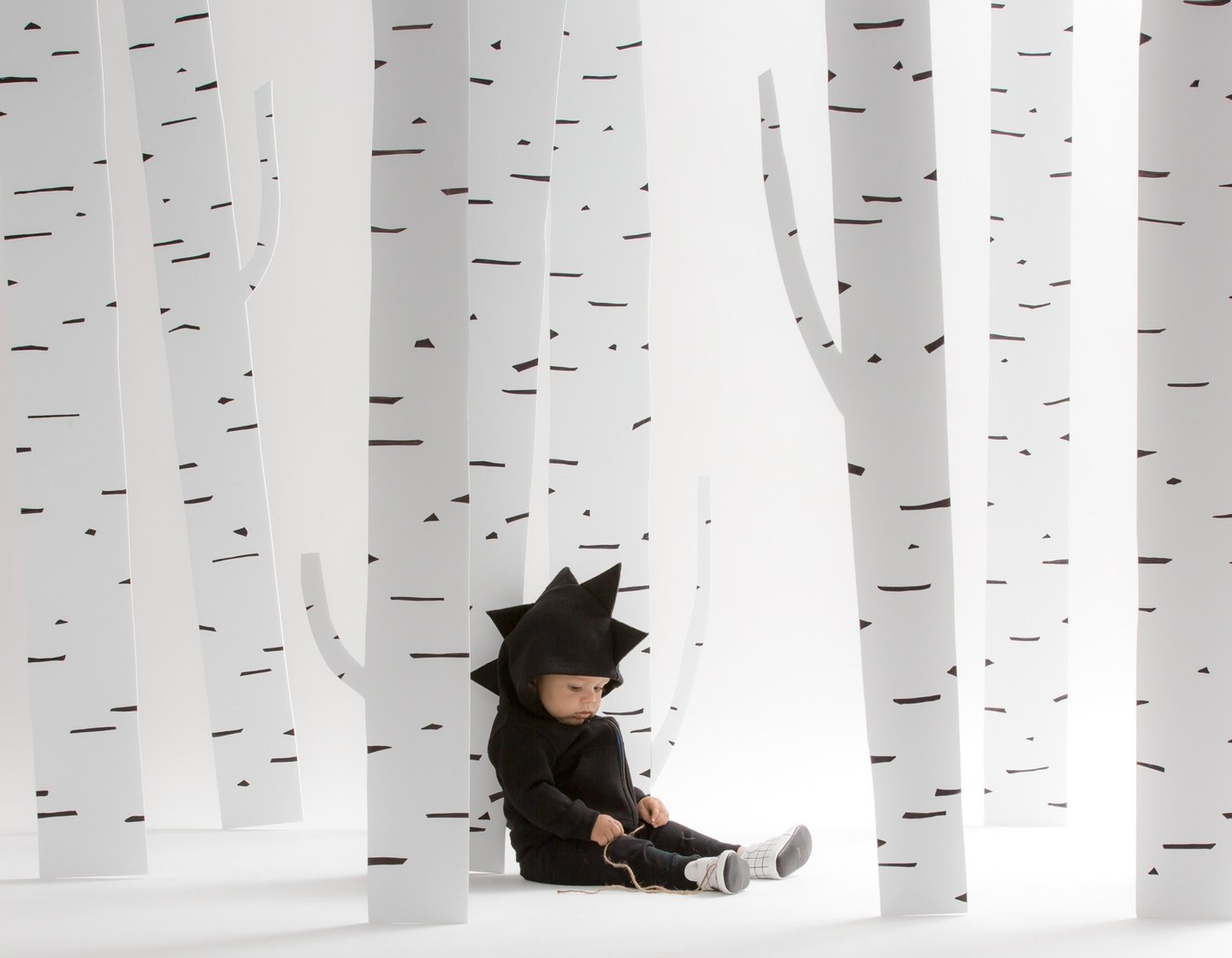 Fashion campaign photography - a baby in a black dinosaur outfit sitting by trees