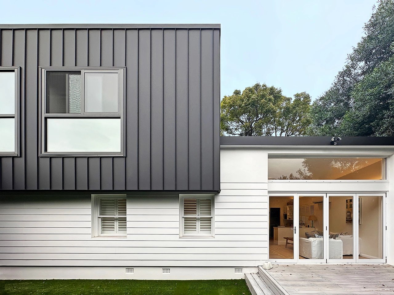 Modern two-story home in Maroubra with a striking black upper floor cantilevered over white weatherboard lower level.