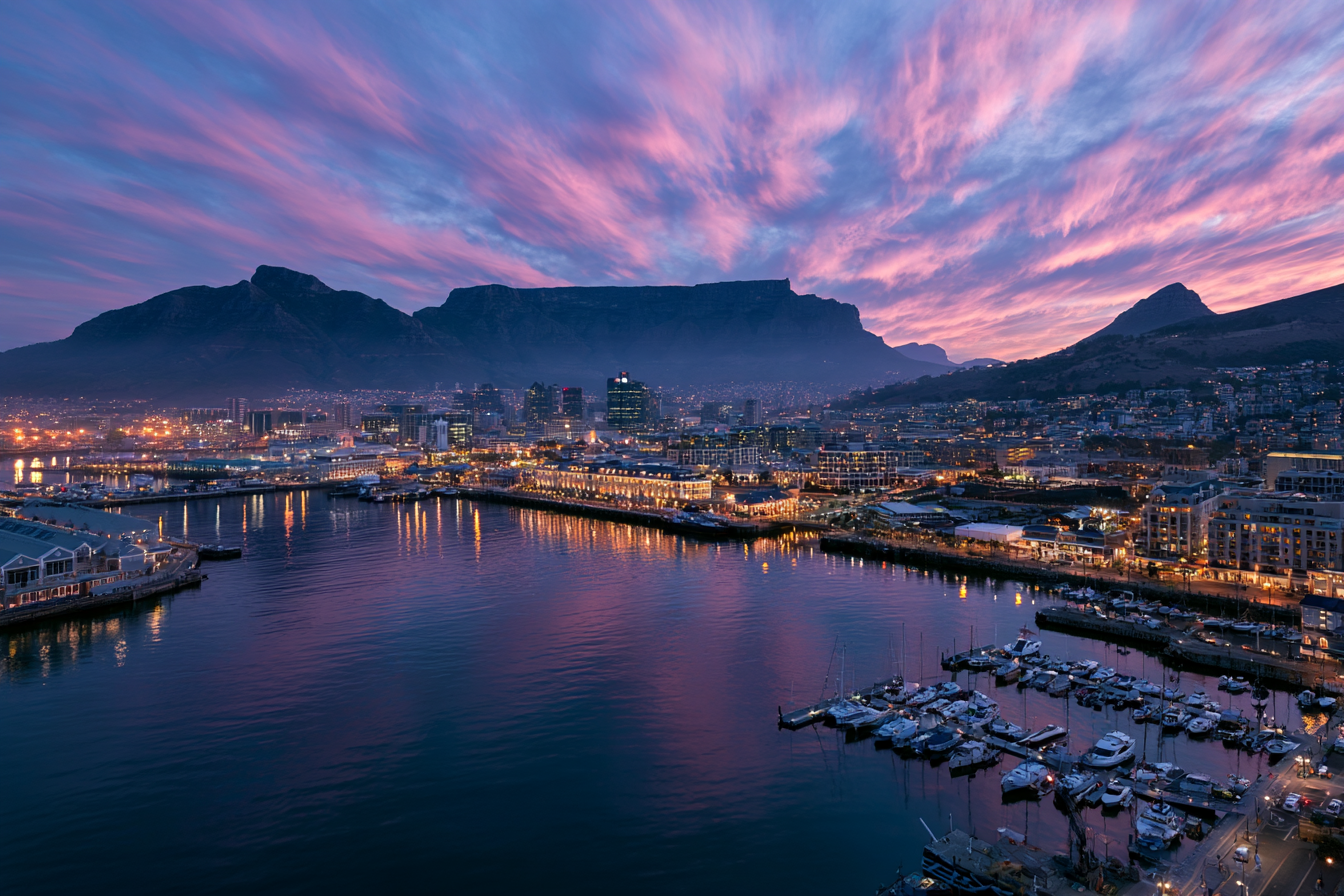 Cape Town V&A Waterfront and harbor at sunset with Table Mountain under a pink sky.