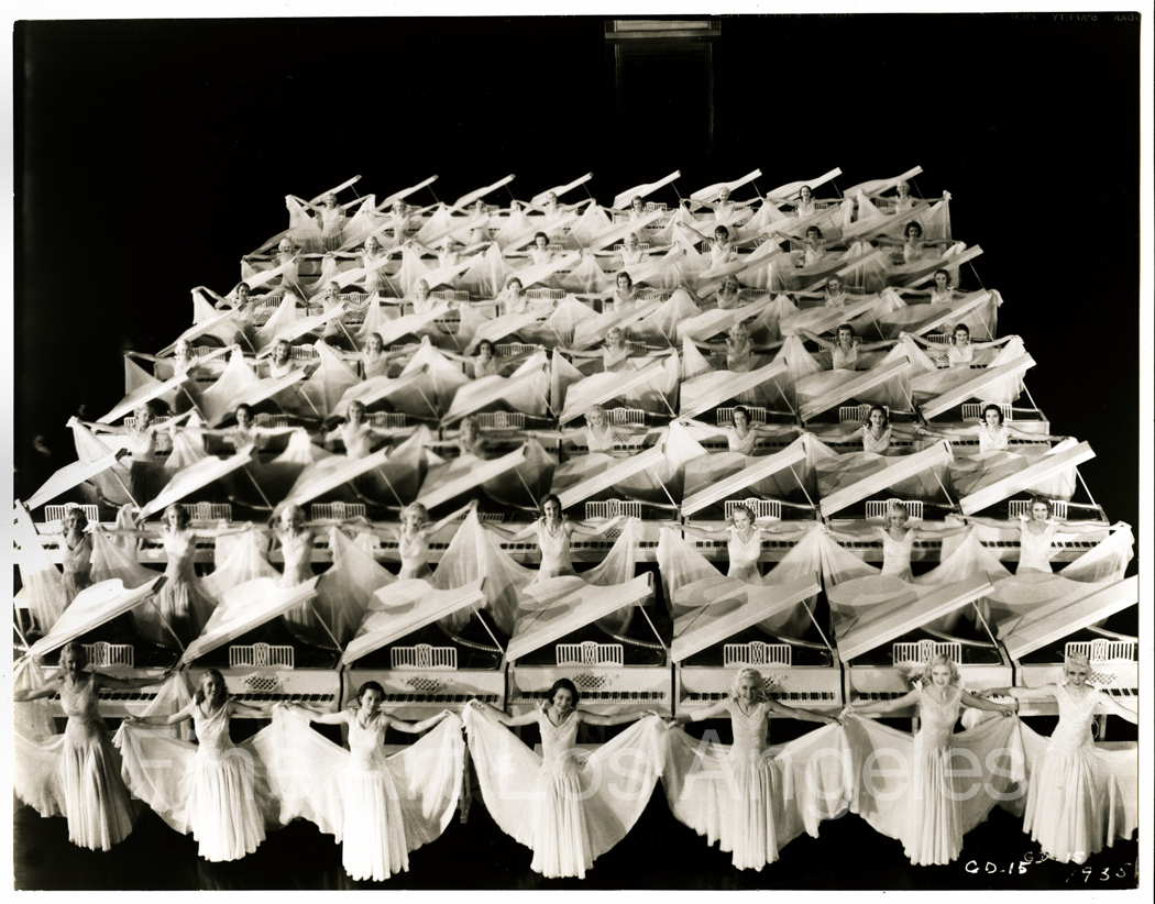 Multiple rows of white grand pianos with white‑clad chorus girls in a Busby Berkeley black‑and‑white
