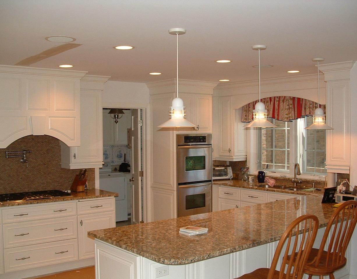Modern white kitchen with granite countertops, stainless steel double oven, and hanging pendant lights over a large island.