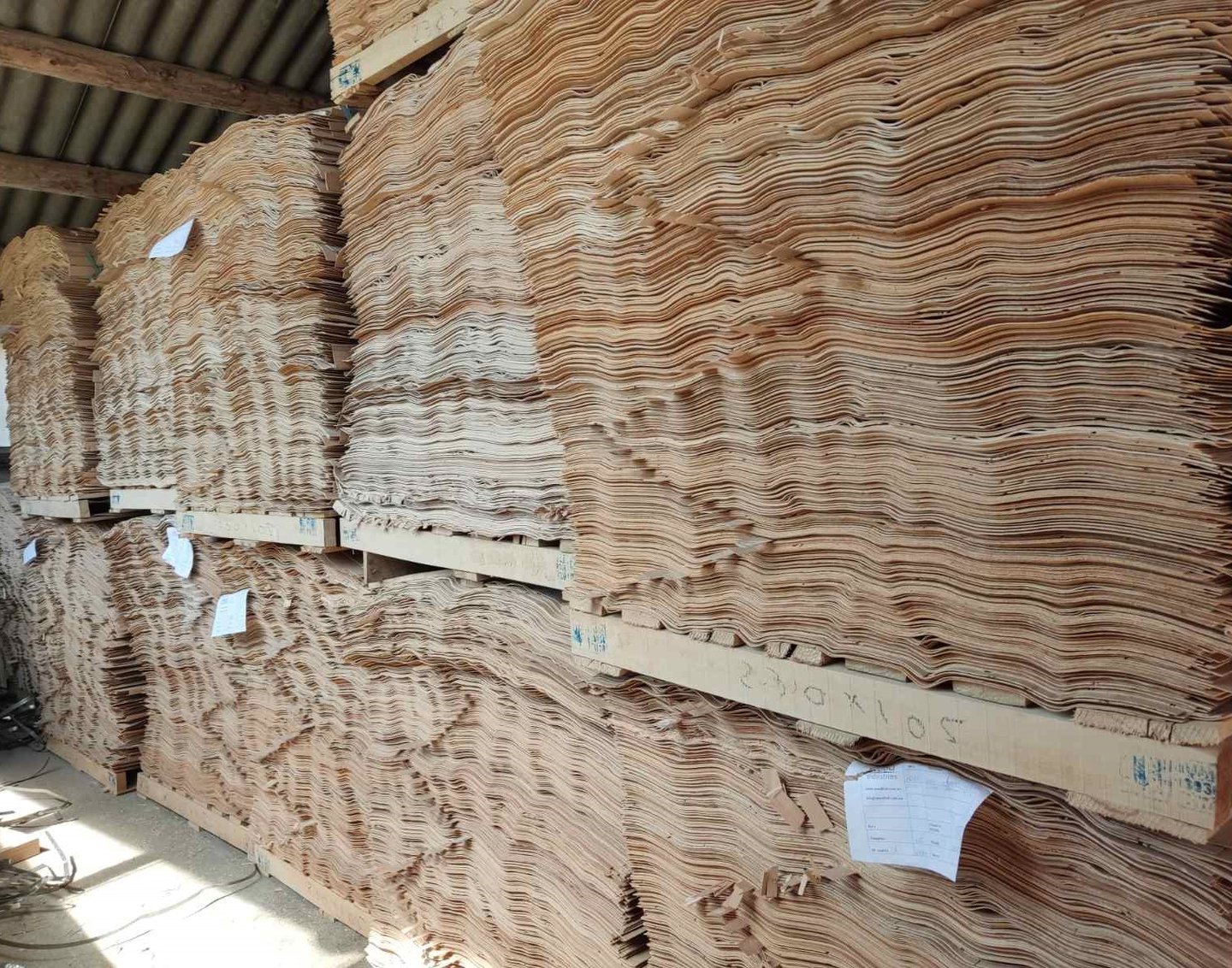 Stacked thin wood veneer sheets on pallets in a lumber manufacturing warehouse.