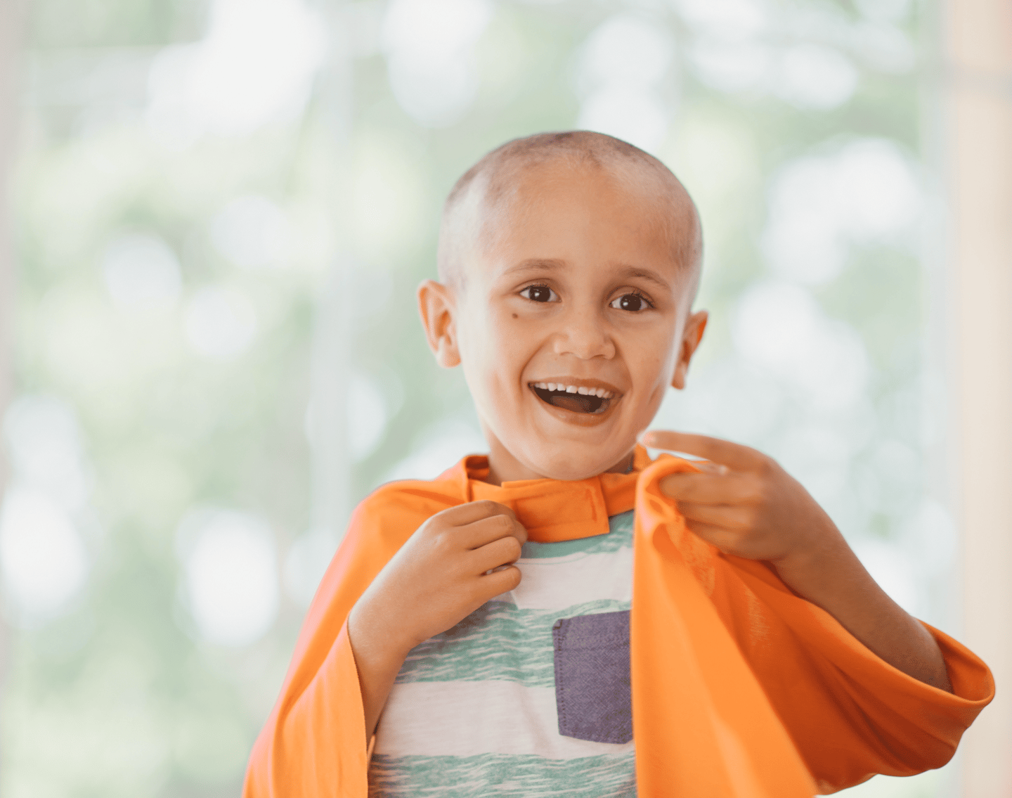 Criança que está passando pelo tratamento contra o câncer brincando com uma capa laranja