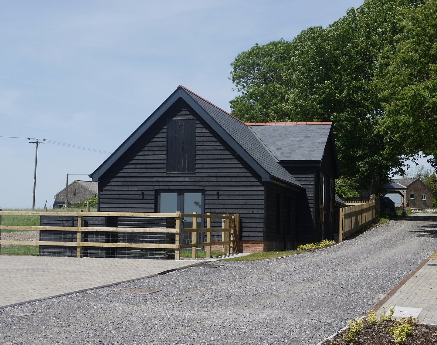 A modern black timber-clad barn conversion with a slate roof and wooden post-and-rail fencing.