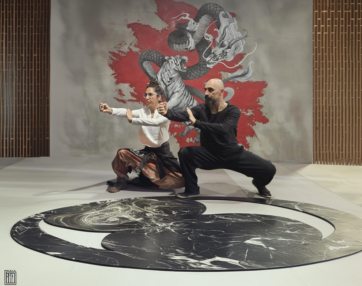 Ismet Himmet and Gizem Kara practicing a Tai Ji form on a yin-yang mat before a dragon mural.