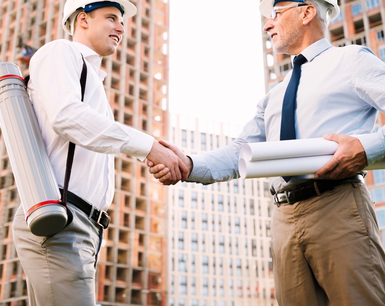 Bir şantiye alanında birbirinden memnun olan ve el sıkışan iki adamın fotoğrafı.