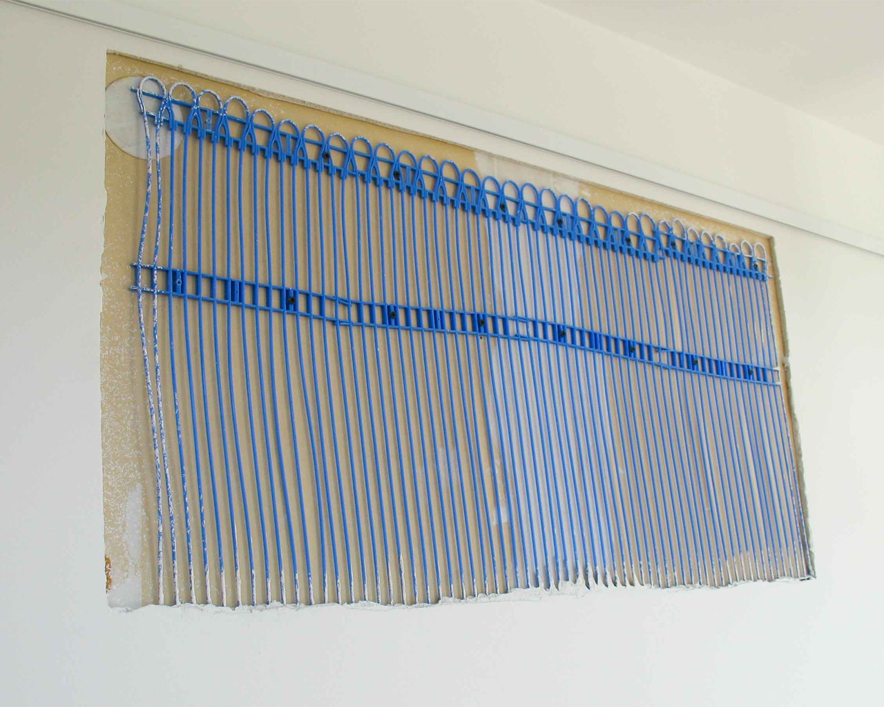 Indoor wall heating installation with blue capillary tubes integrated into the wall surface.