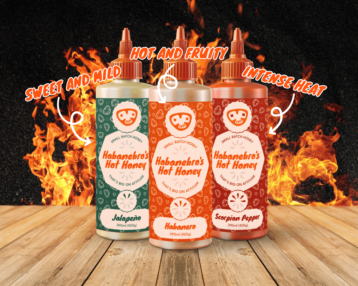 Three squeezy hot honey bottles on a wooden table, with flames in the background.
