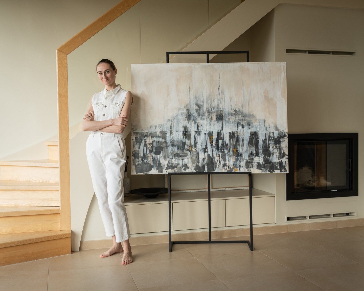 A female artist in white denim posing next to her large abstract painting on an easel.