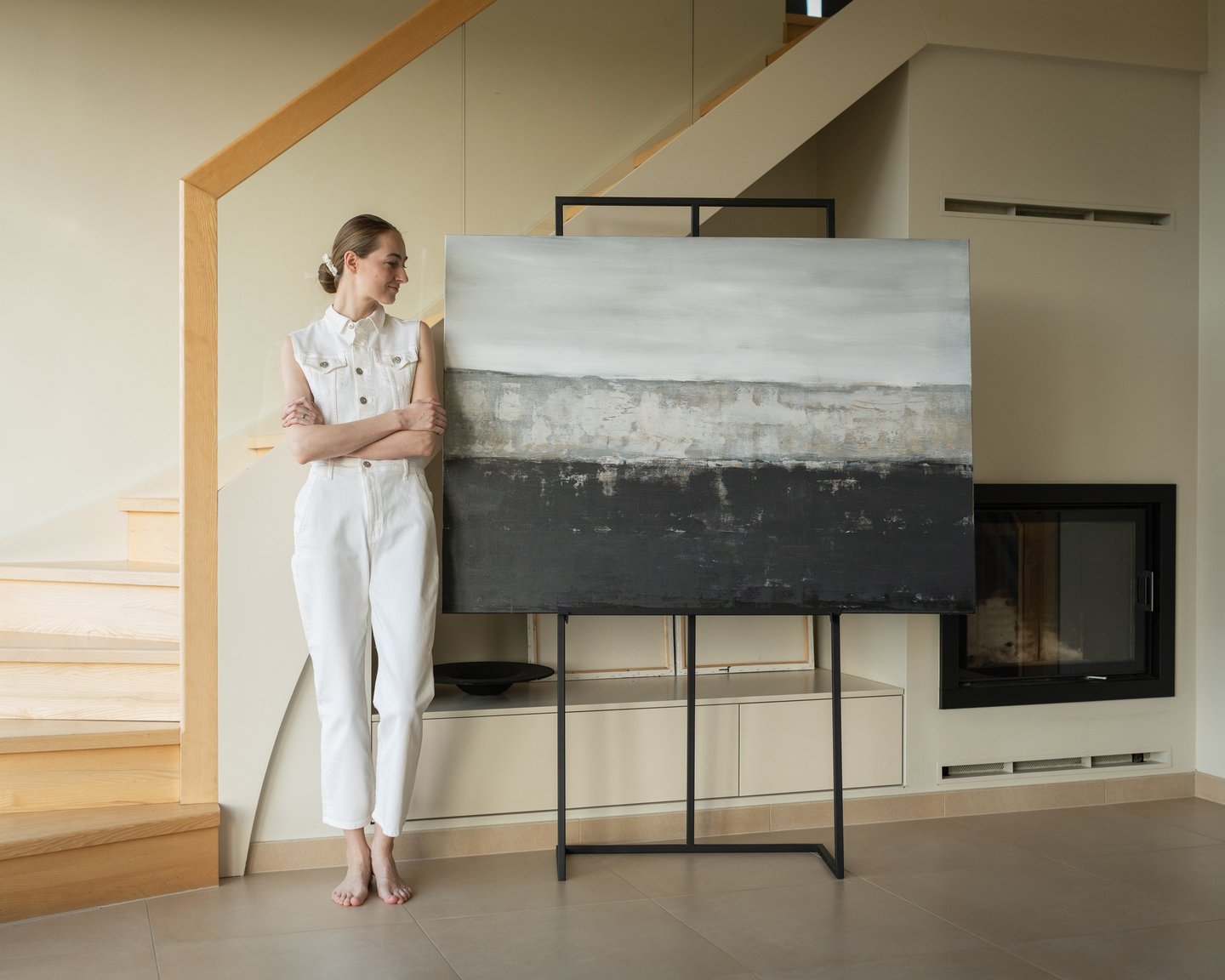 Artist standing by large abstract landscape painting on an easel in a modern minimalist living room.