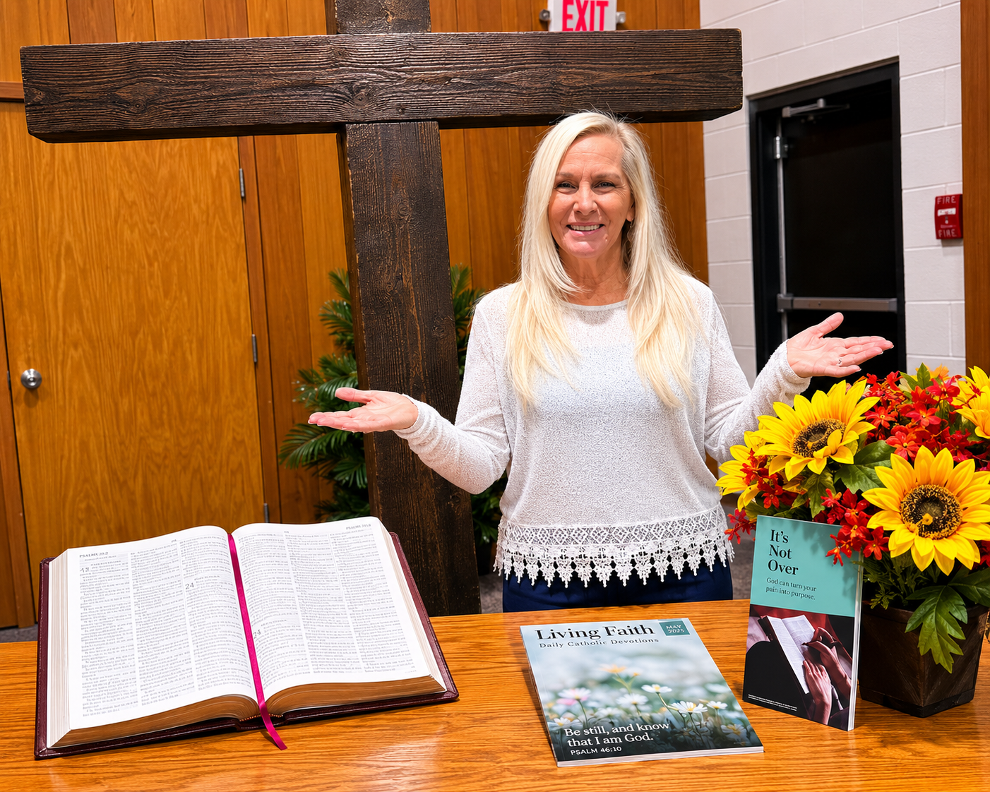 Myra Lee standing by a wooden cross with an open Bible and Daily Catholic Devotions book.