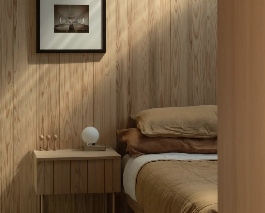Minimalist bedroom with light wood paneling, a wooden nightstand, and linen bedding in warm earthy tones.