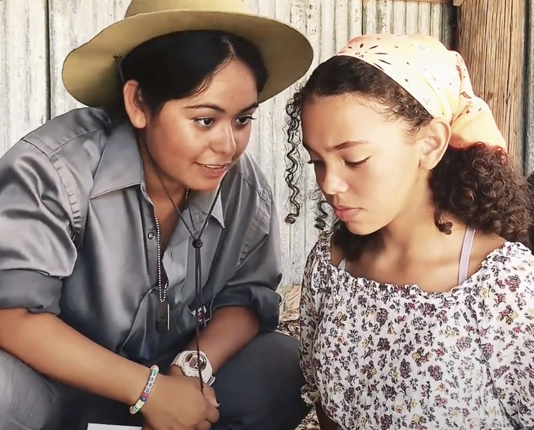 a young woman in a sheriff hat speaking to and a teen girl in a head scarf