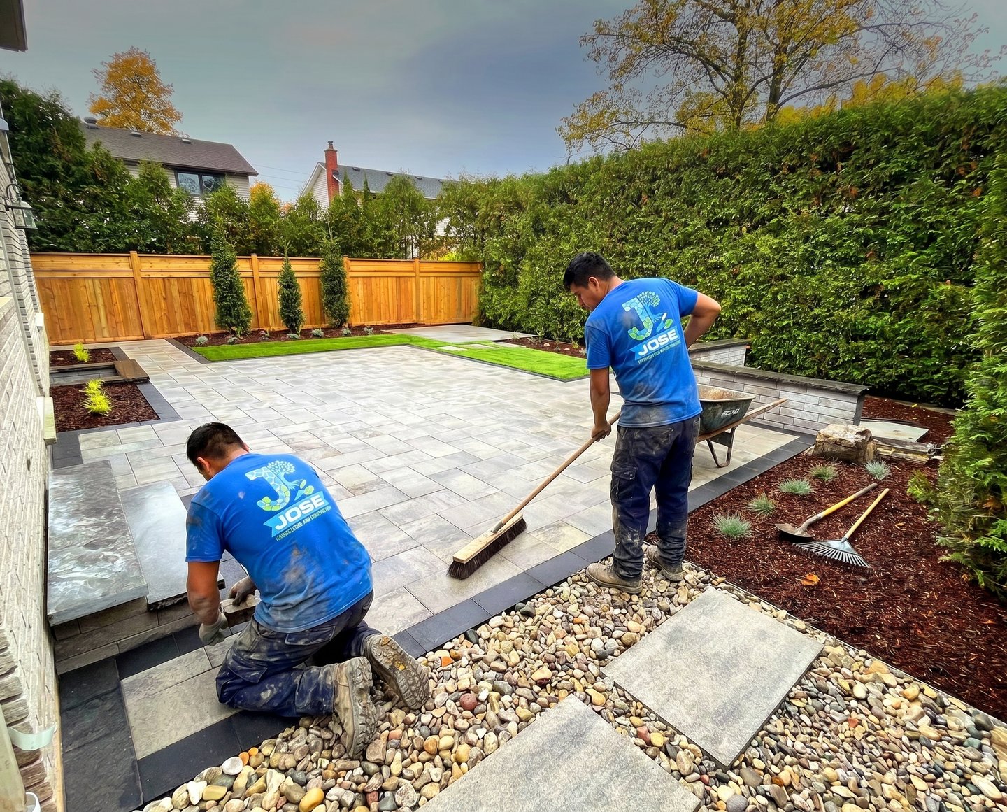 Professional landscapers installing a custom stone paver patio and backyard garden beds In New York