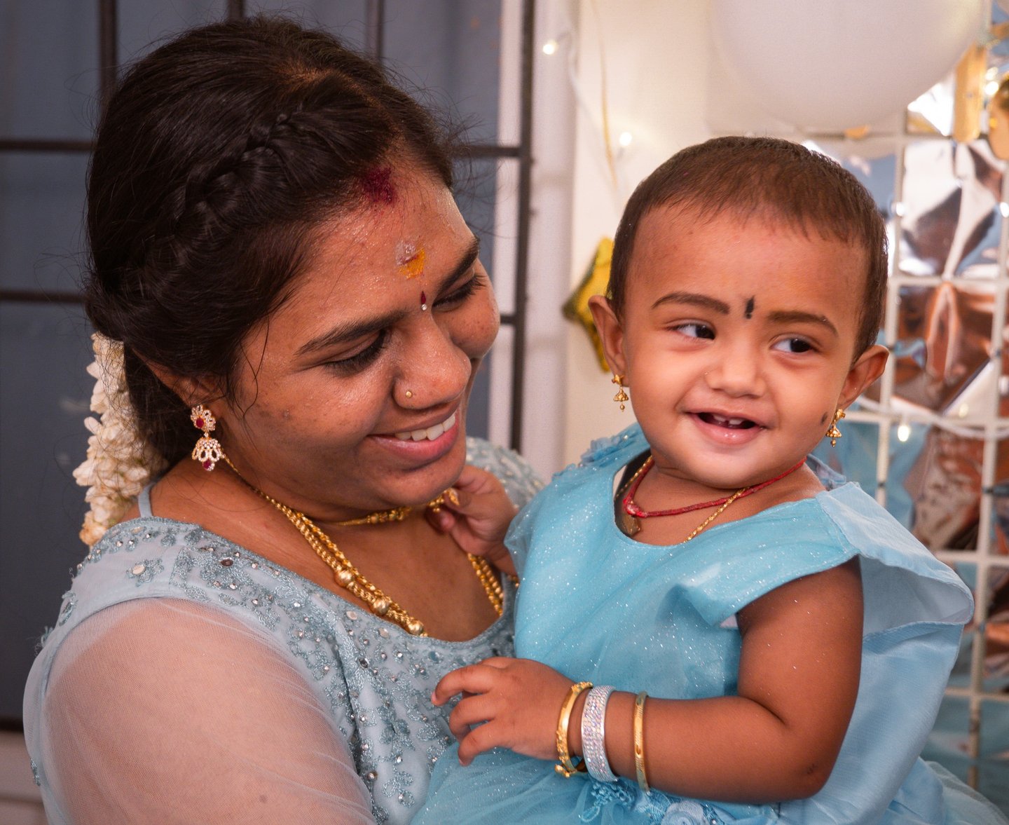 A mother in a blue lehenga holding her baby daughter at a first birthday celebration, photographed b