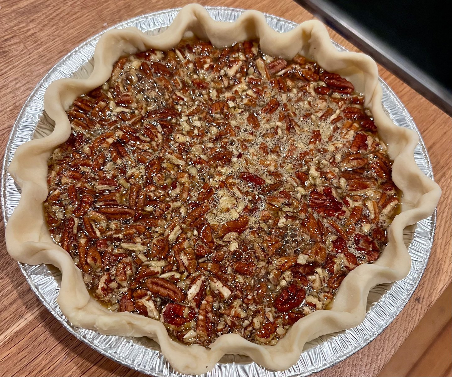 Freshly prepared unbaked pecan pie with a fluted crust in a silver foil tin on a wooden table.
