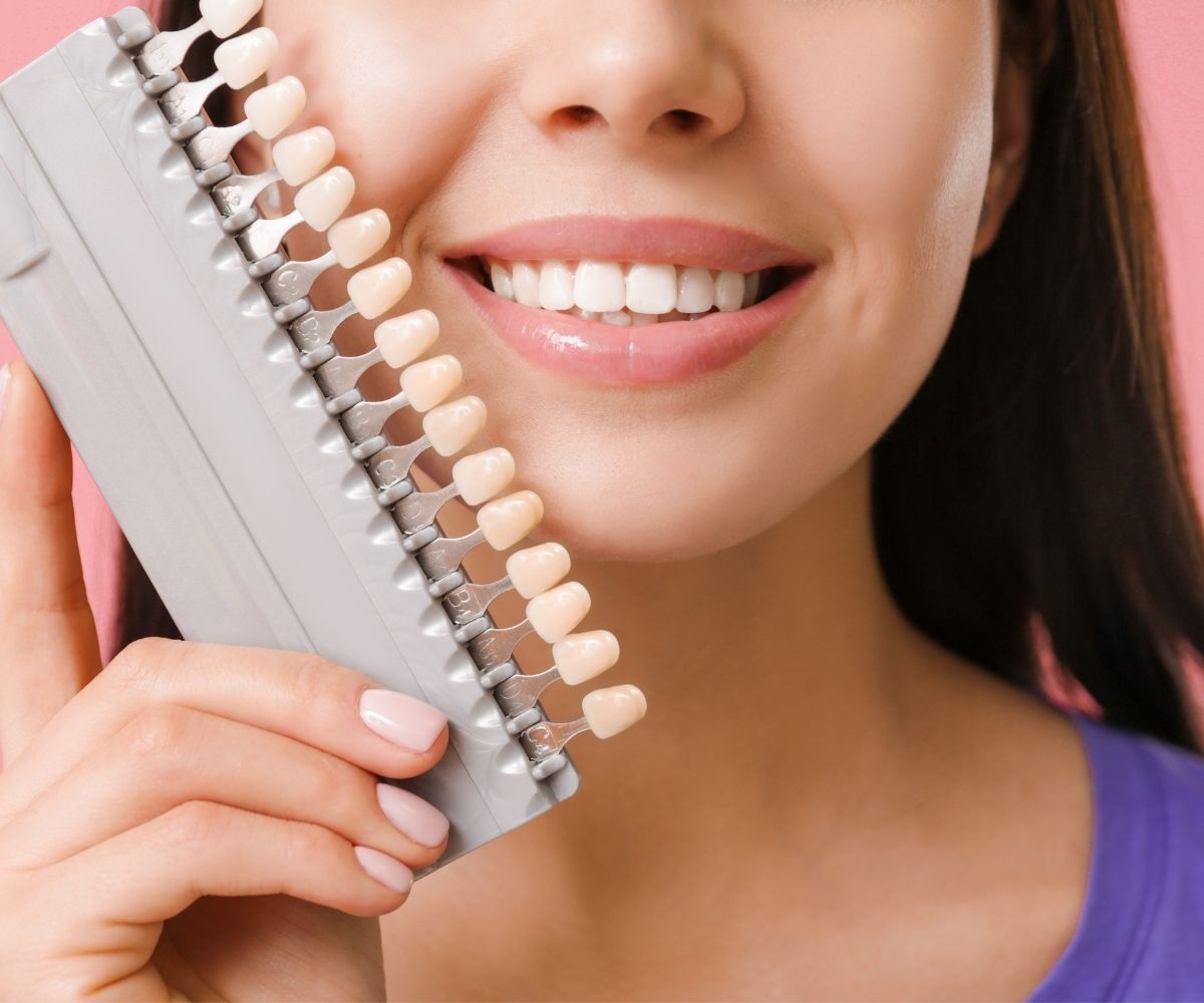 A smiling woman holding a tooth shade comparison model next to her mouth.