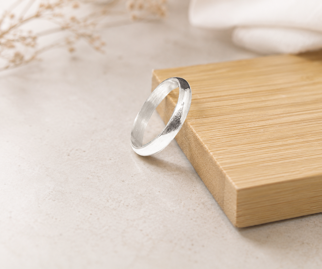 Polished 999 fine silver wedding band resting on a bamboo wood block with a minimalist aesthetic.