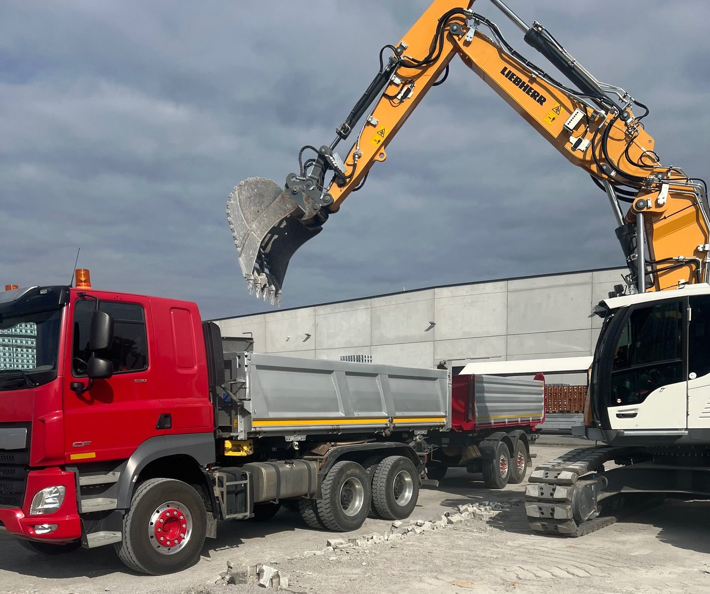 A yellow Liebherr excavator loading debris into a red dump truck at a construction site.