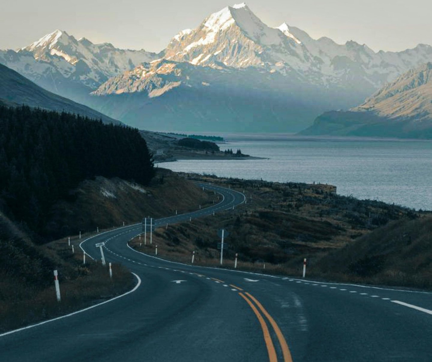 Winding mountain road leading toward snow-capped Mount Cook and Lake Pukaki in New Zealand.