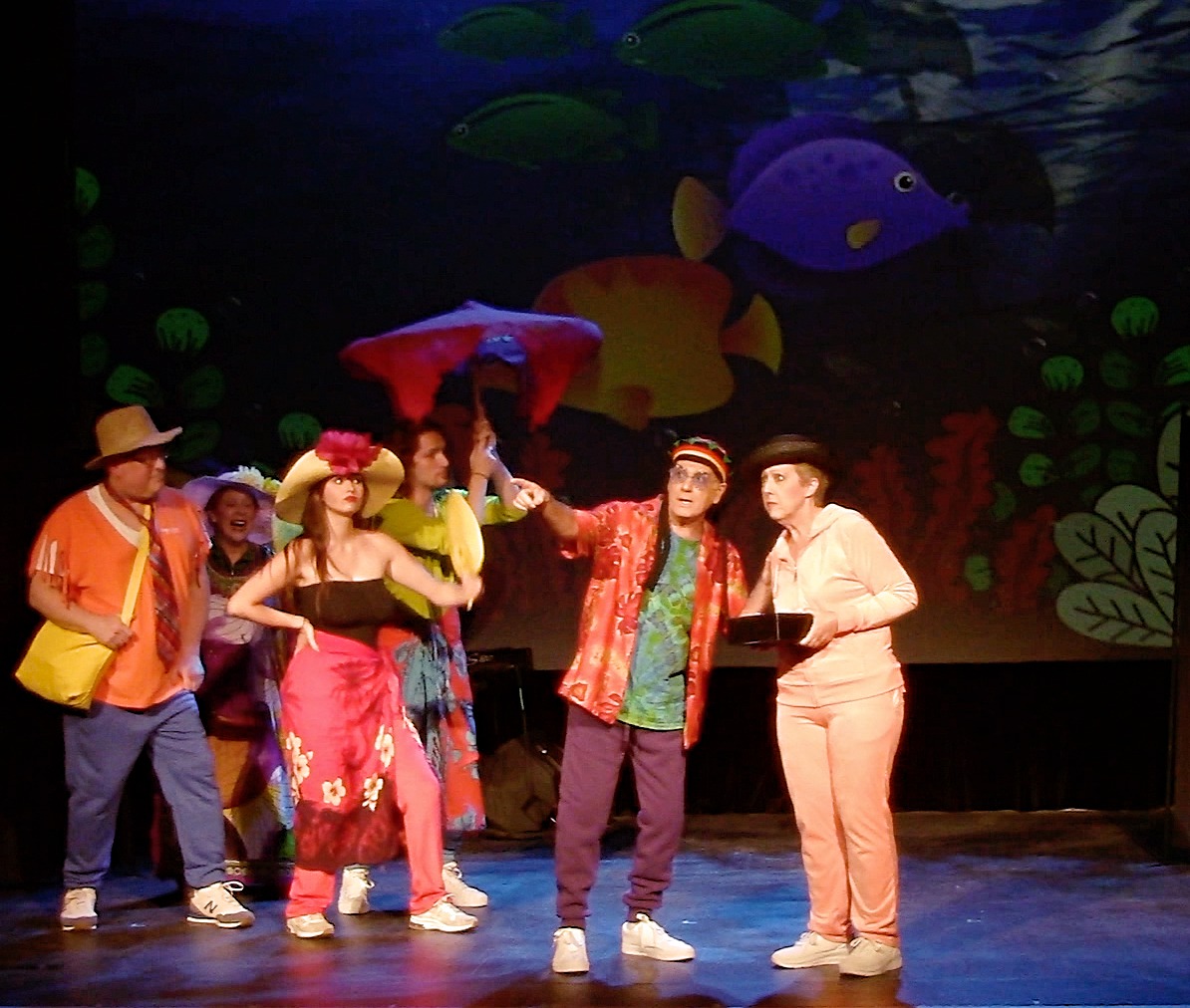 Actors in colorful costumes perform a comedy musical number with a tropical fish backdrop.
