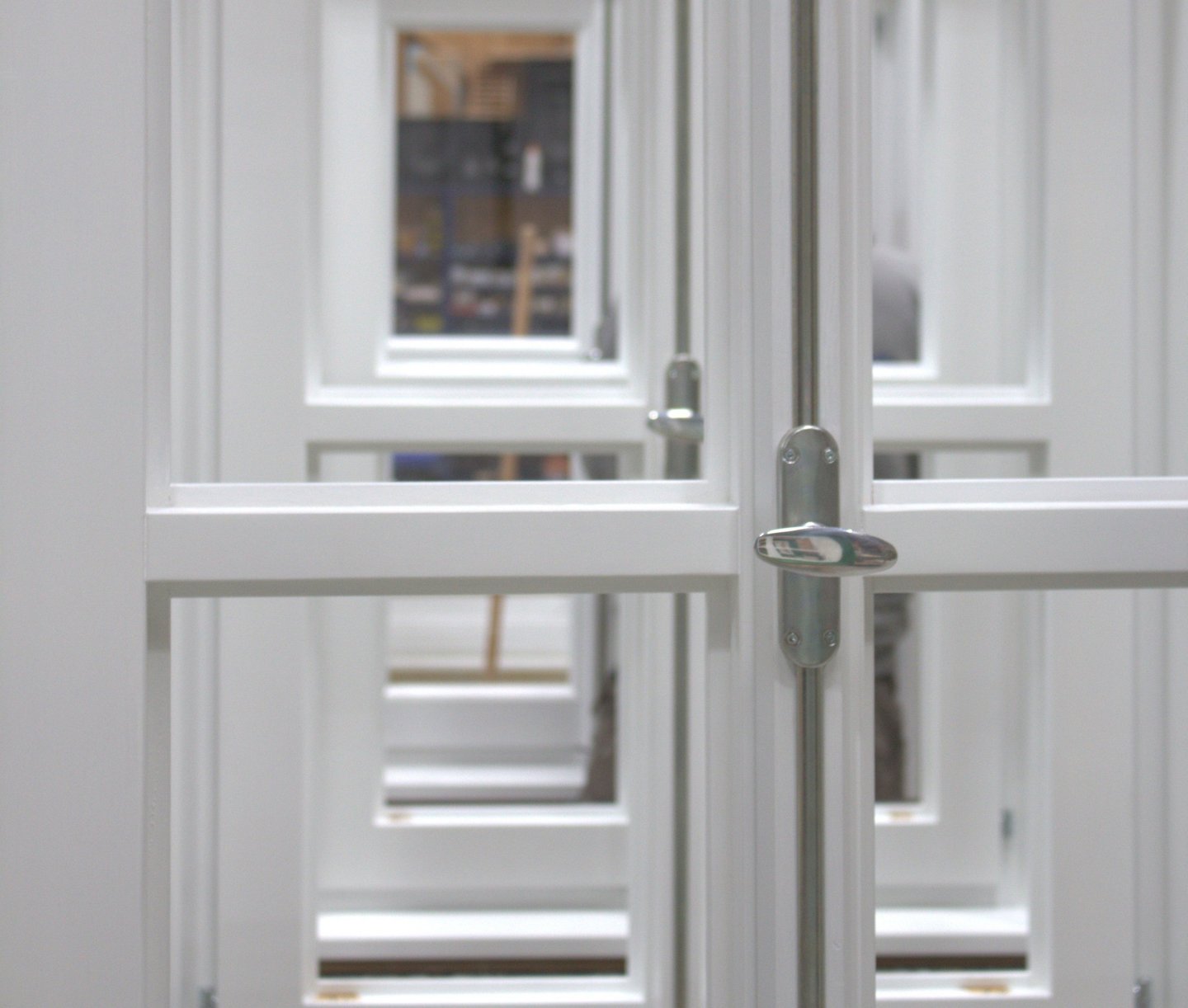 etailaufnahme weiß lackierter Holzfenster mit silbernem Griff und Blick durch mehrere Fensterebenen.