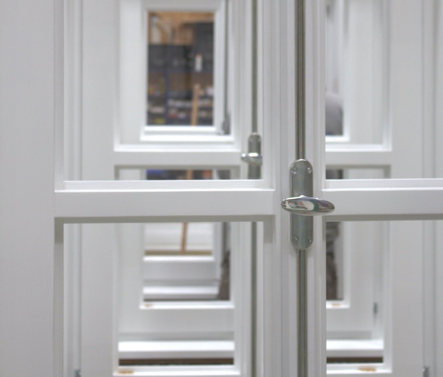 etailaufnahme weiß lackierter Holzfenster mit silbernem Griff und Blick durch mehrere Fensterebenen.