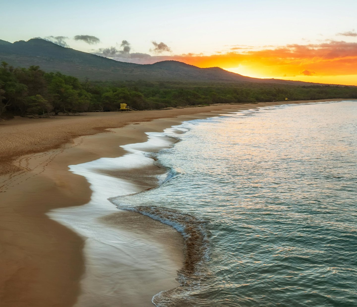 Golden sunset over Makena Beach in Maui with ocean waves washing onto the sandy tropical shoreline.