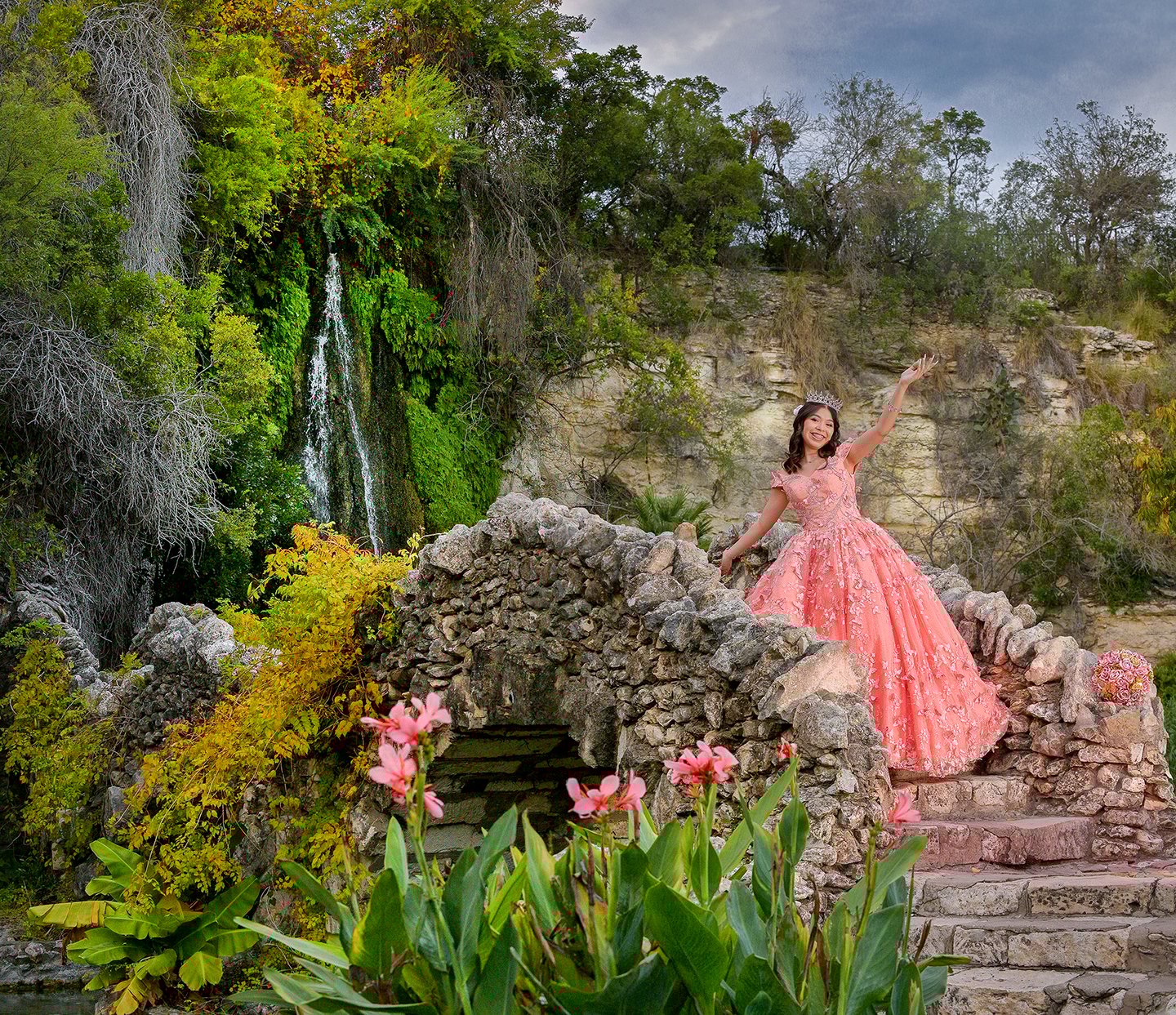 a woman in a pink quinceanera xv dress standing on a stone wall