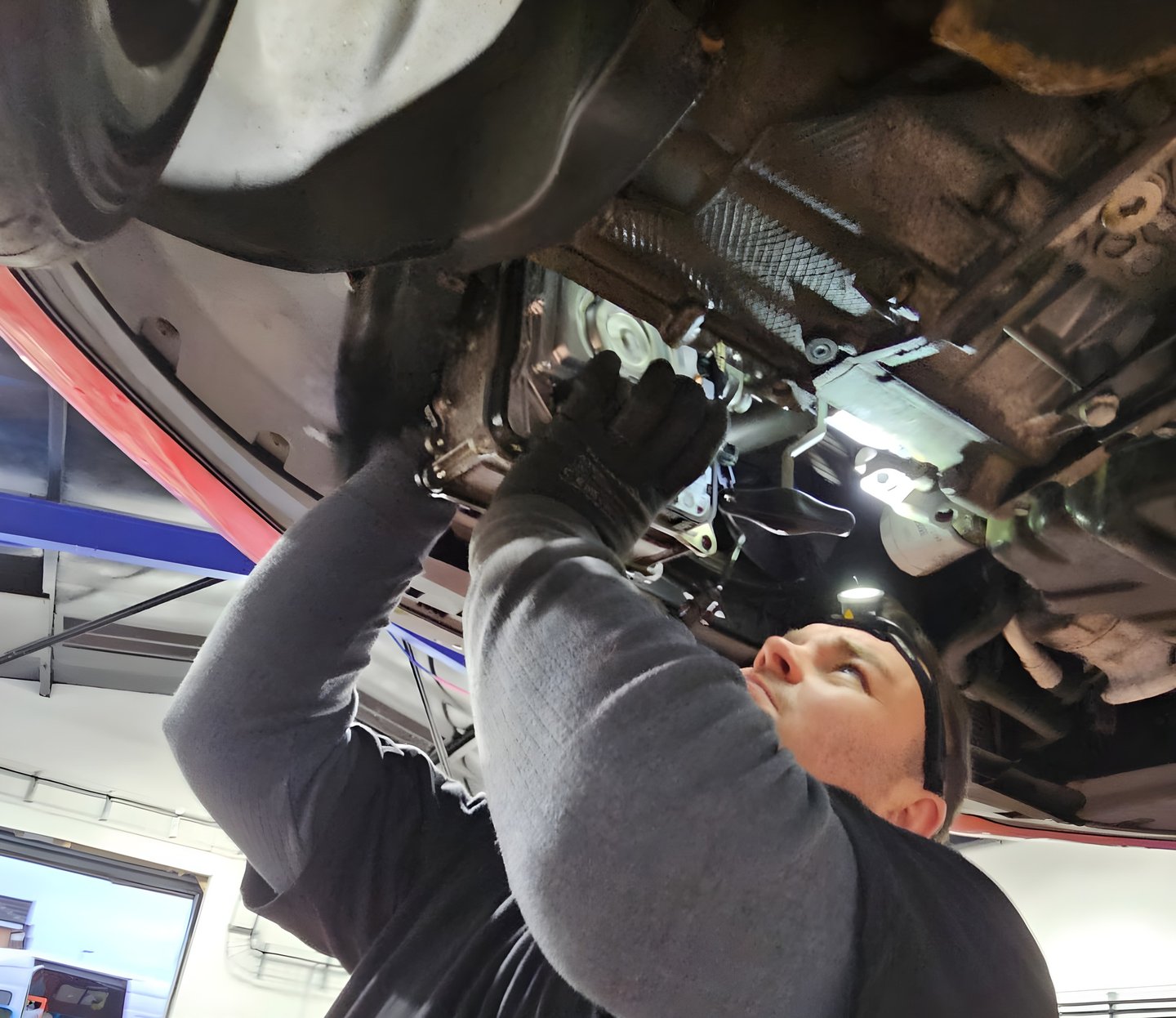 Professional mechanic in a repair shop performing under-car maintenance and transmission service.