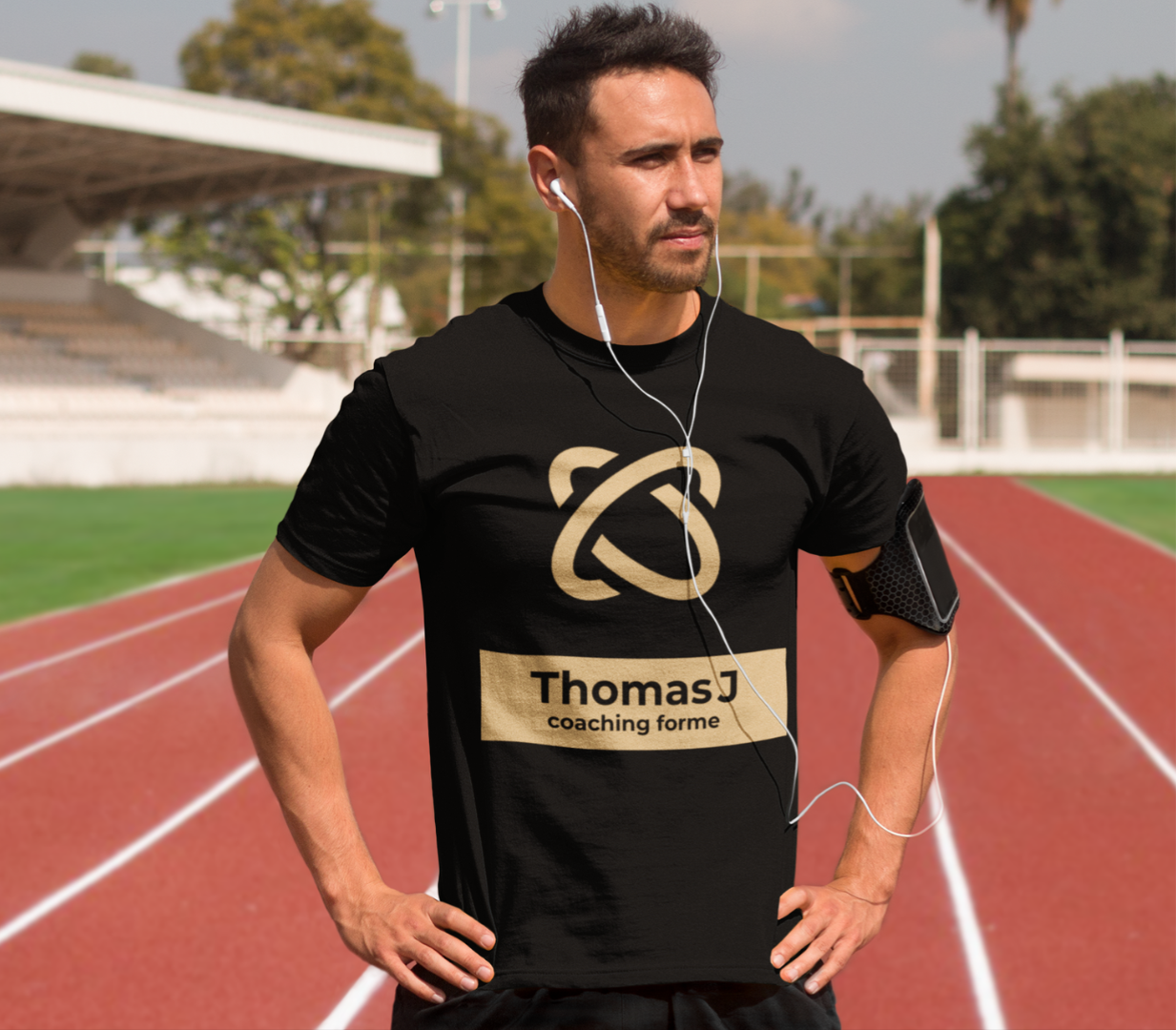 Homme en t-shirt noir avec un logo de coaching forme debout sur une piste de course rouge.