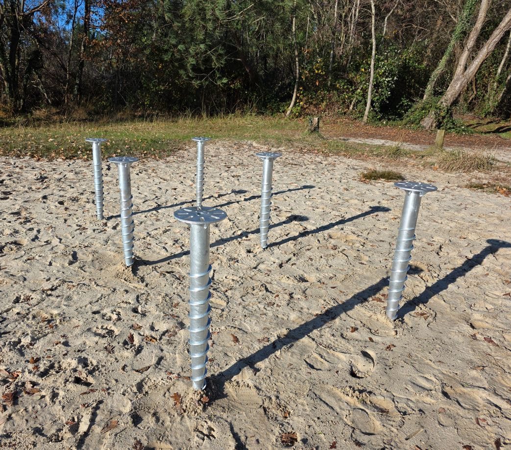 Plusieurs pieux vissés installés dans le sable pour un chalet bois