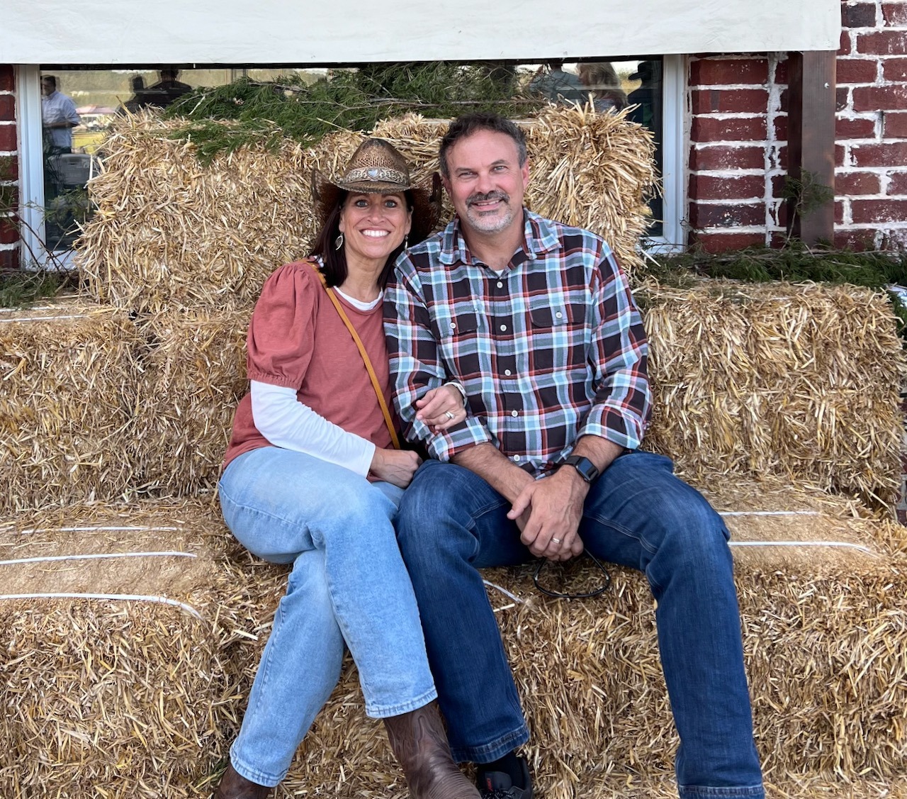 Monica Weaver and her husband smiling and sitting on bales of hay