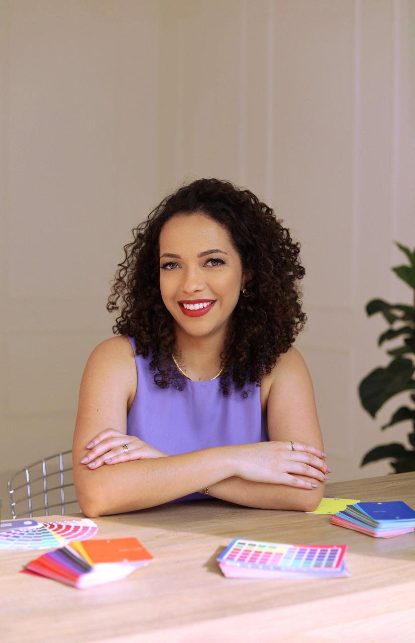 Mulher cacheada sorridente com braços cruzados, oferecendo serviços de coloração pessoal