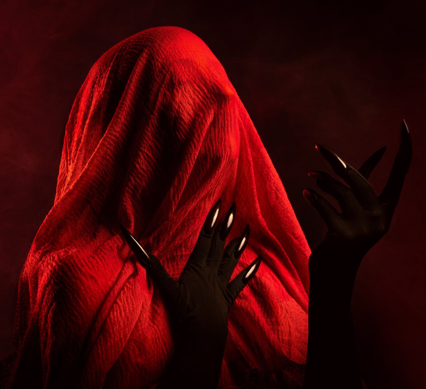 Fotografía artística de moda con modelo cubierto por tela roja y uñas negras dramáticas